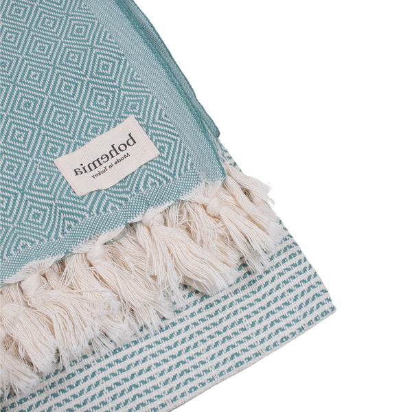 A cotton towel in a mint color with an intricate design and white fringe.