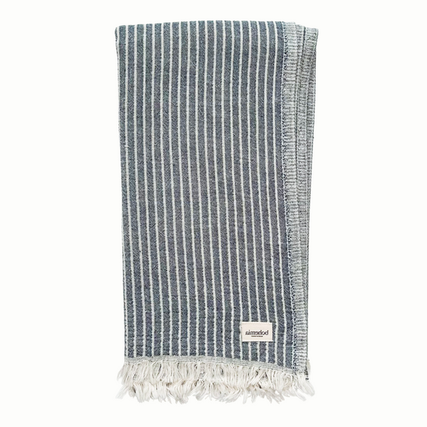 A cotton towel in an indigo color and subtle striped pattern with a white fringe.