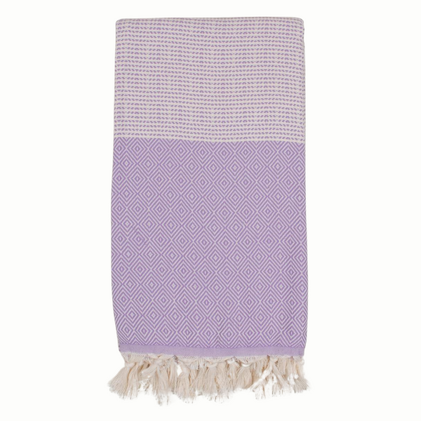 A cotton towel in a lavender color with an intricate design and white fringe.