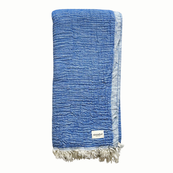 A cotton muslin towel in a rich blue color with a white fringe.