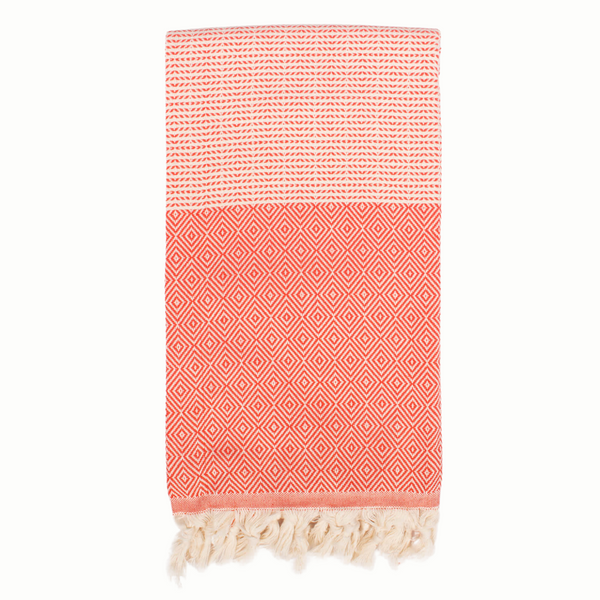 A cotton towel in a tangerine color with an intricate design and white fringe.