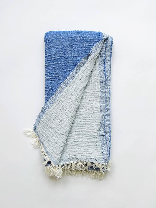 A cotton muslin towel in a rich blue color with a white fringe.